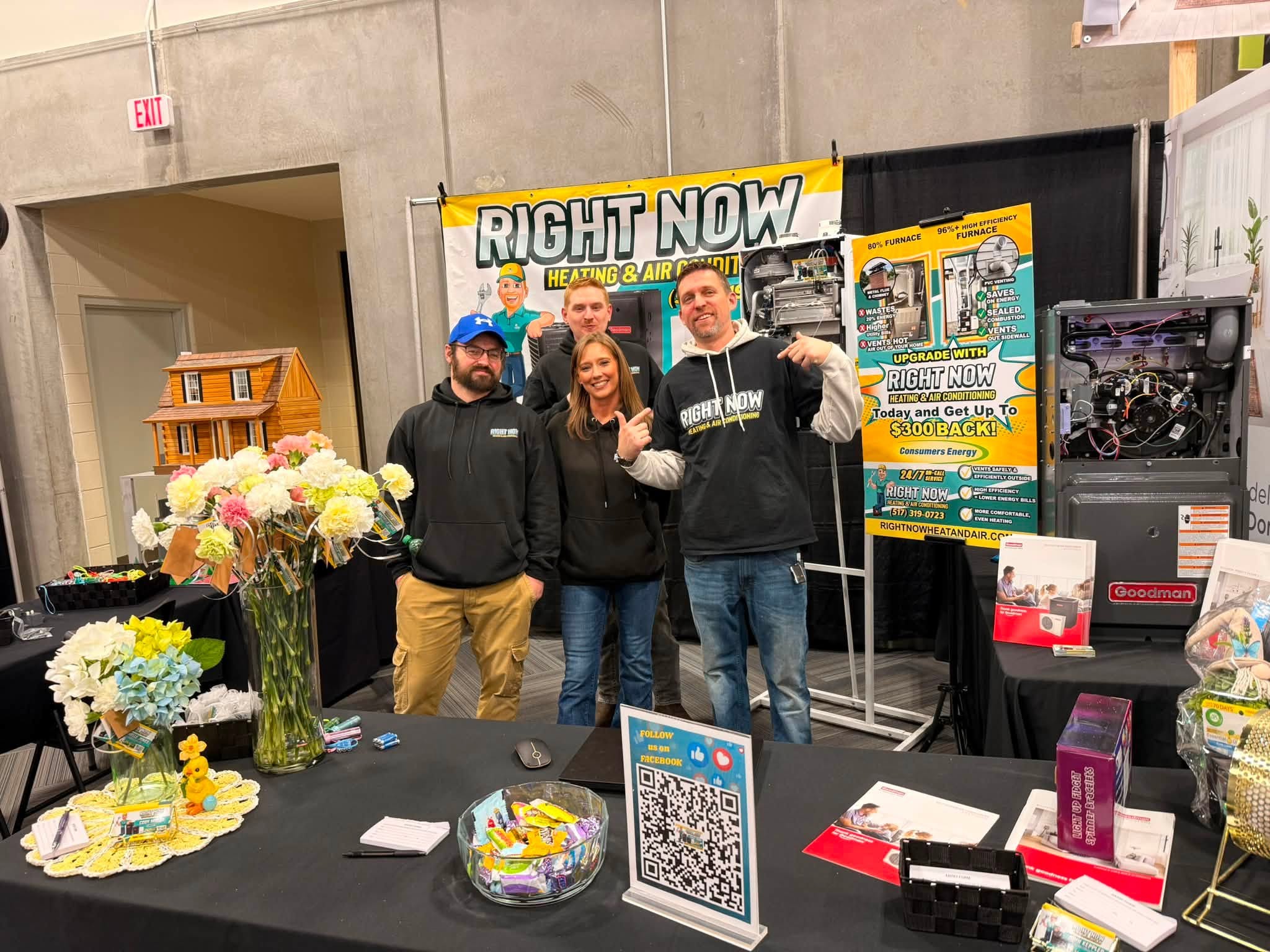 Four people stand at a trade show booth for “Right Now Heating & Air,” surrounded by promotional materials, flowers, and product displays.