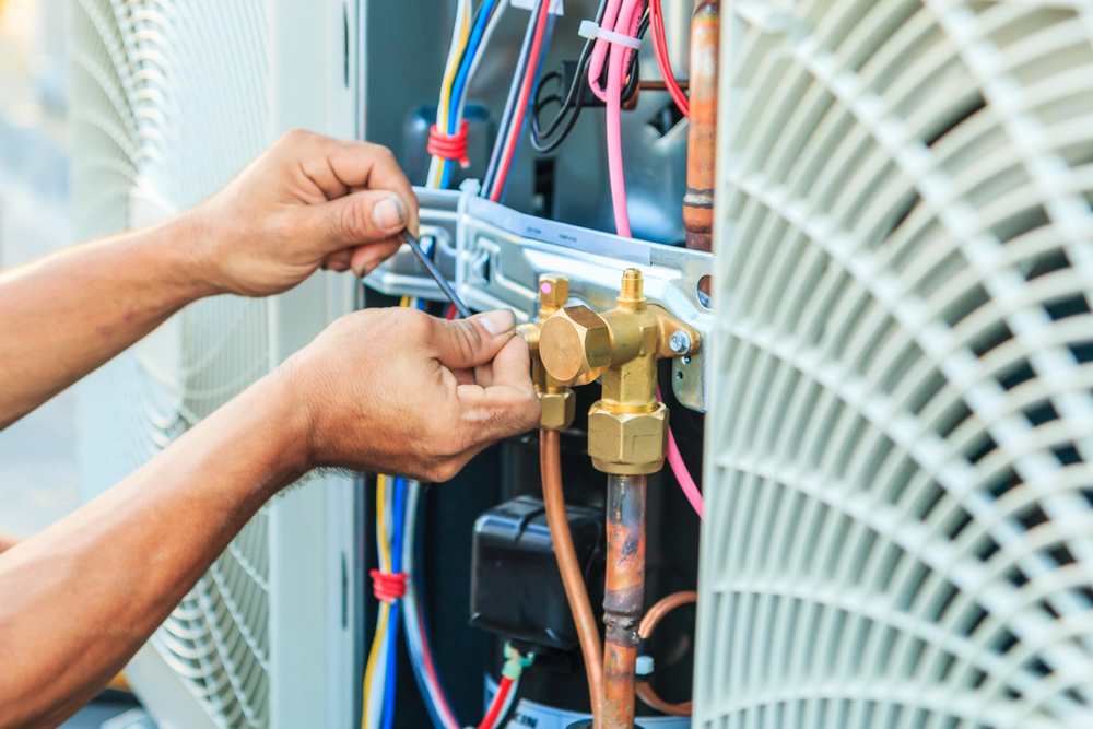 Close-up of hands repairing or installing an air conditioning unit, adjusting wires and pipes with tools.