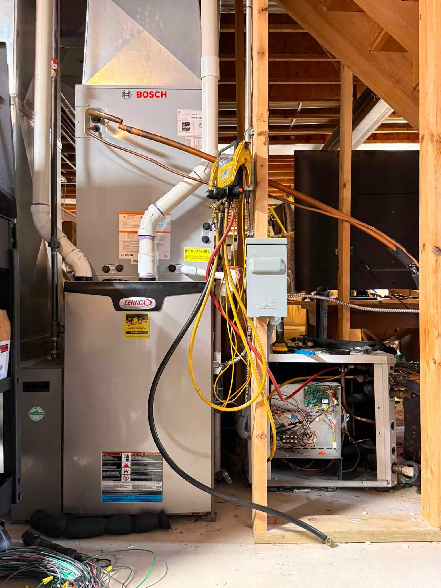 A basement workshop with a Bosch furnace, wiring, exposed pipes, open fuse box, and HVAC equipment; unfinished walls and ceiling are visible.