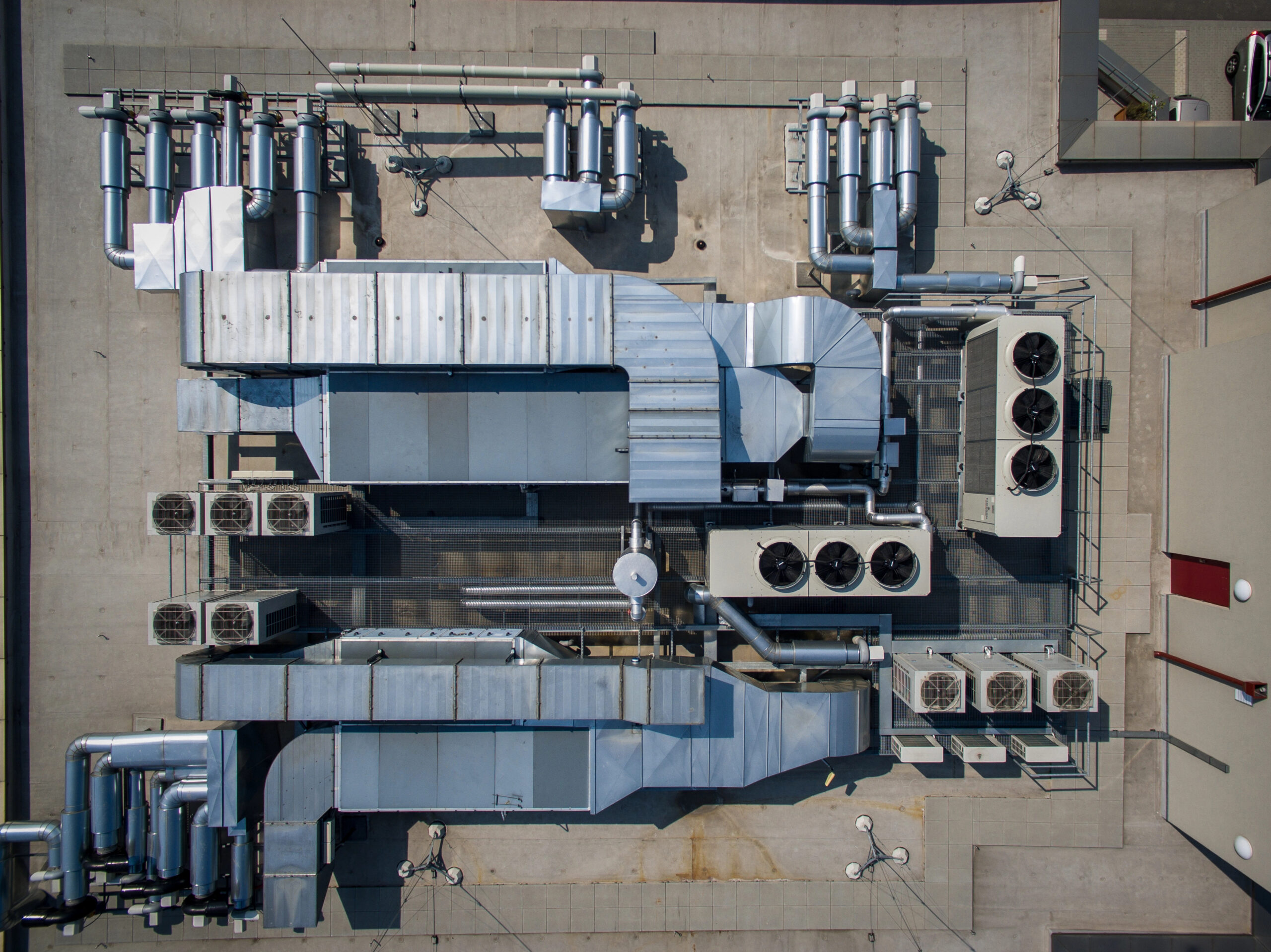 Aerial view of an industrial rooftop with HVAC units, ducts, vents, and various piping systems on a concrete surface.