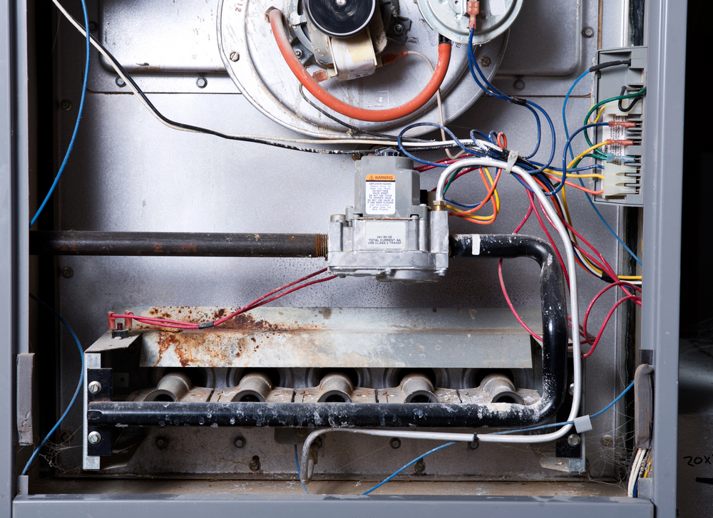 Close-up of the interior components and wiring of a gas furnace, showing burners, pipes, and electrical connections.