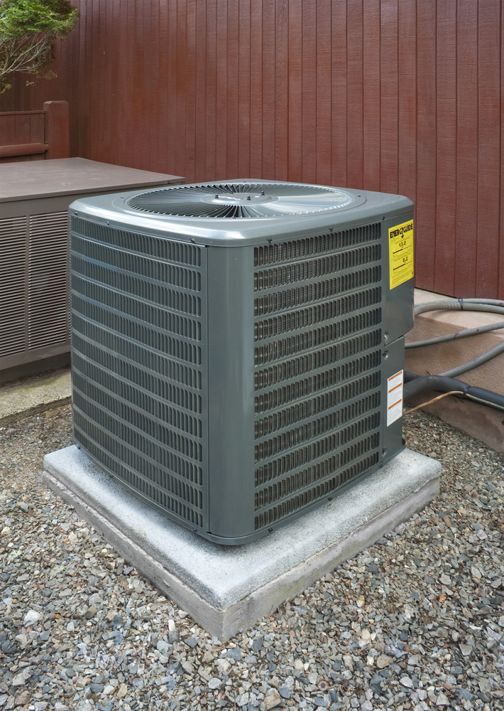 Outdoor air conditioning unit on a concrete pad, surrounded by gravel, with a brown wooden fence and another unit in the background.