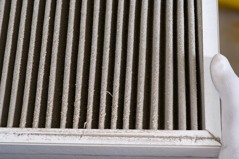 A close-up of a hand holding a dirty air filter with visible dust and debris trapped in the pleats.