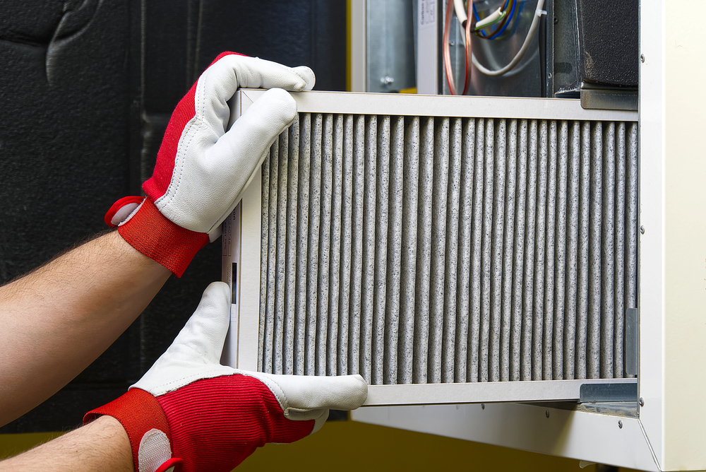 Person wearing red and white gloves is installing or removing a pleated air filter from a residential HVAC system.
